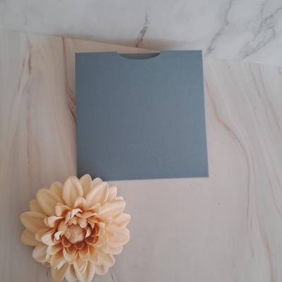 Envelope azul texturizado com flor artificial creme sobre superfície de padrão mármore.