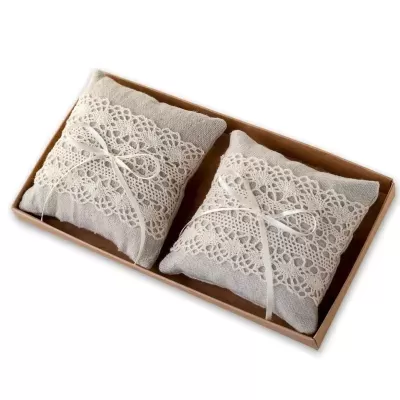 Duas almofadas cinza claro com renda branca e laços numa caixa de cartão