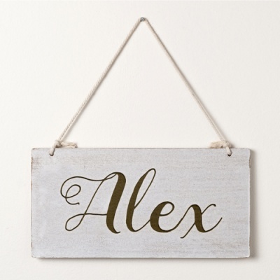 Placa de madeira branca com texto 'Alex' em letra cursiva castanha pendurada por corda