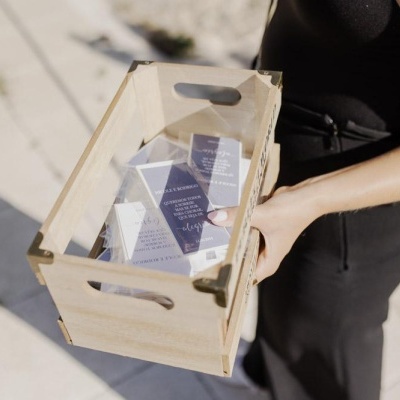 Caixa de madeira com cartões escuros com texto branco, segurada por pessoa de roupa preta