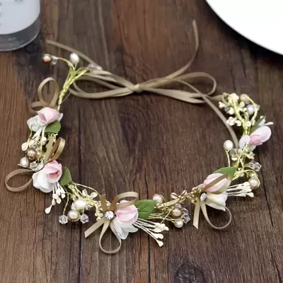 Grinalda com flores cor-de-rosa e brancas, folhas verdes e pérolas sobre mesa de madeira