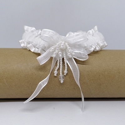 Liga branca com babados e laço de pérolas sobre cilindro de cartão