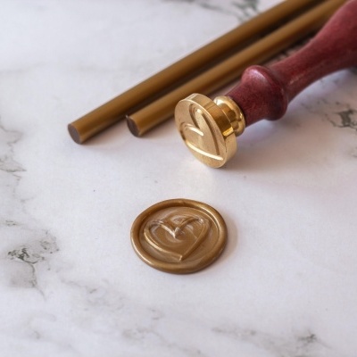 Selo lacre metálico dourado com cabo de madeira vermelha e cera lacrada dourada.