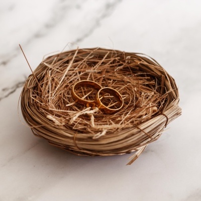 Duas alianças douradas num ninho de palha sobre superfície branca de mármore