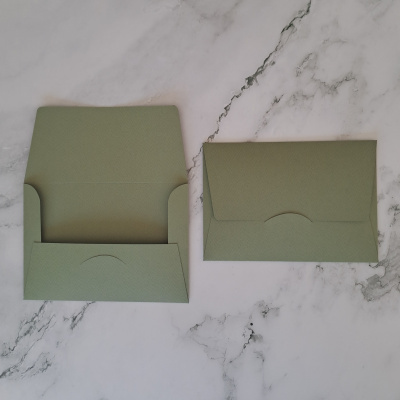 Dois envelopes verdes com textura sobre superfície branca de mármore.