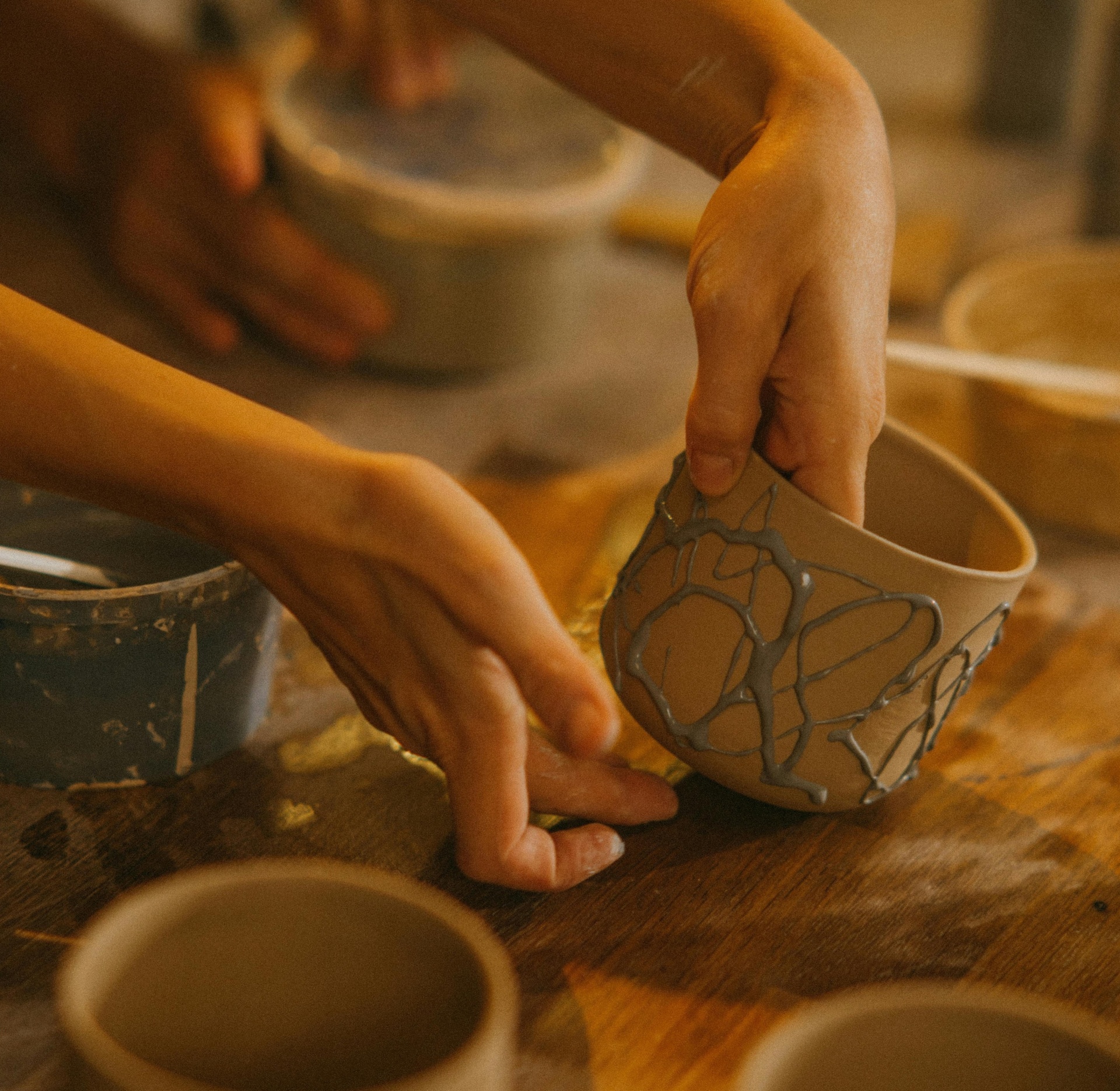 Taça de cerâmica pintada à mão com padrão cinzento e mãos a segurá-la sobre mesa de madeira