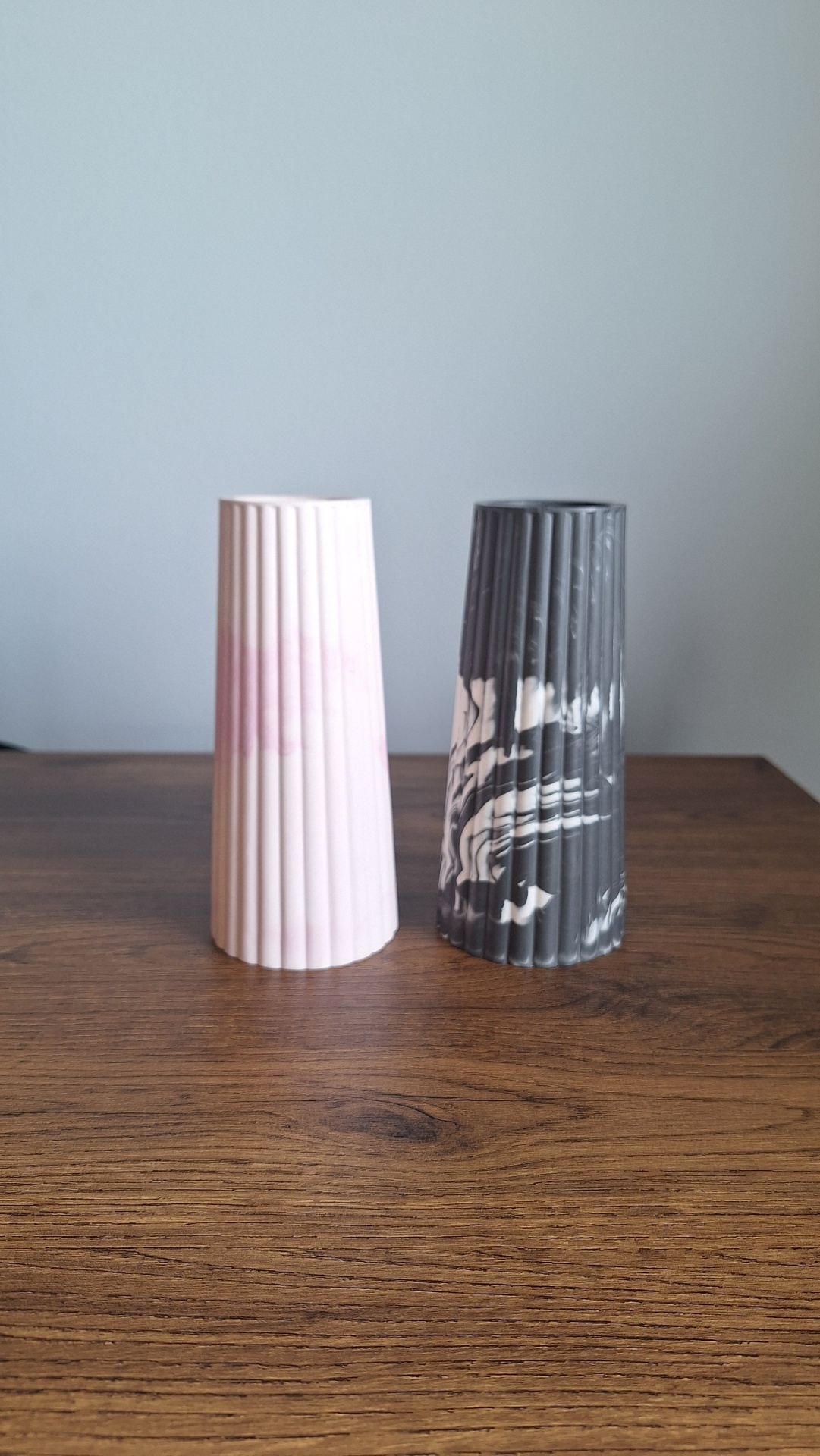 Jarra Dália Esculturas cónicas rosa claro e cinza com padrão marmoreado branco numa mesa de madeira.