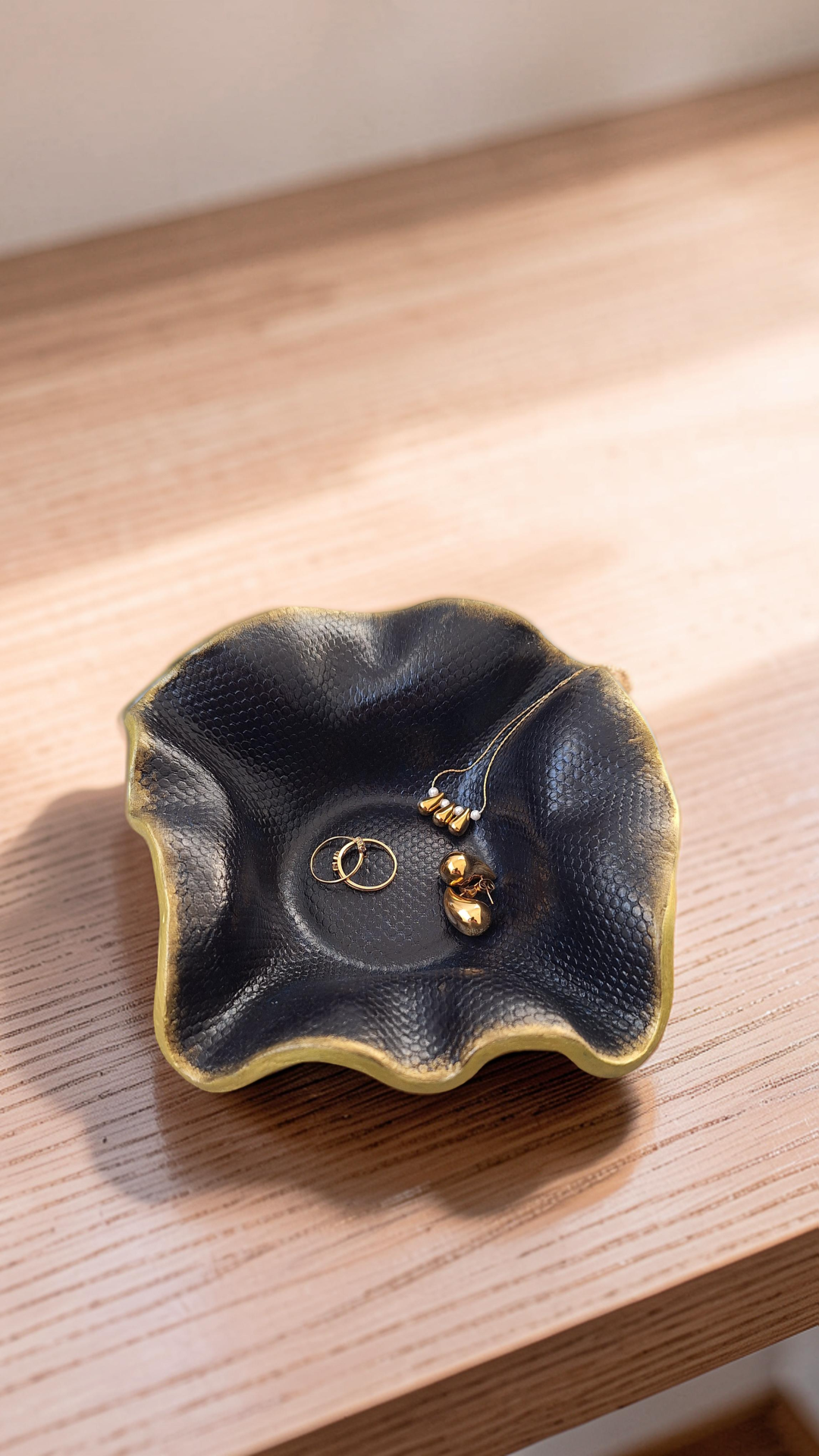 Flor – Peça em Cerâmica Versátil para Velas ou Joias Taça decorativa preta com textura de pele de serpente e bordas douradas com joias douradas dentro, sobre madeira clara.