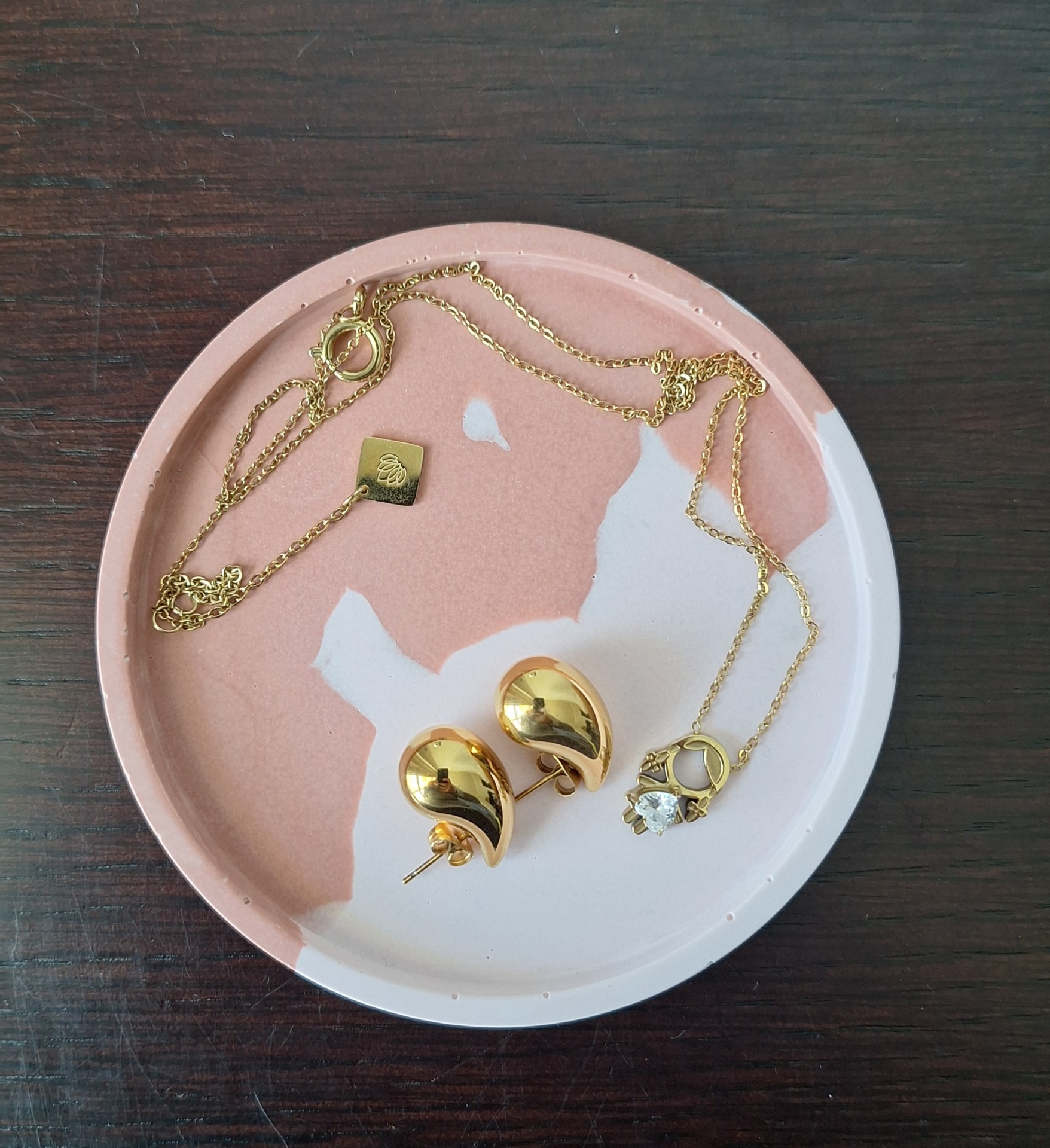 Como Criar Peças em Jesmonite: Dicas Para Iniciantes Colar dourado com pendente de pedra e brincos dourados num prato de cerâmica rosa e branco