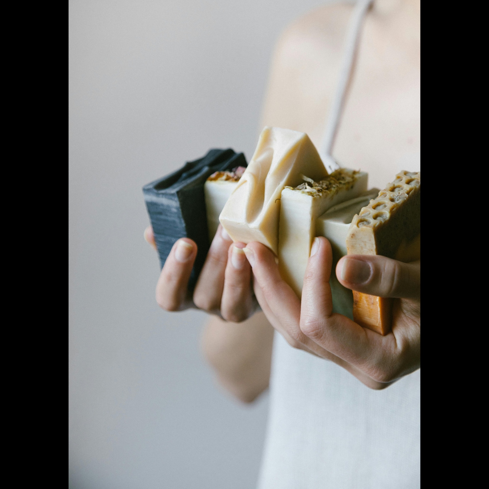 Por que escolher produtos naturais para o corpo e cabelo? Mãos segurando barras de sabão artesanal de várias cores e texturas