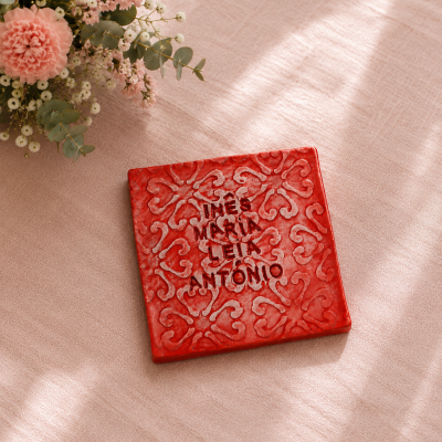 Azulejo vermelho decorativo com texto recortado sobre tecido rosa com flores ao lado