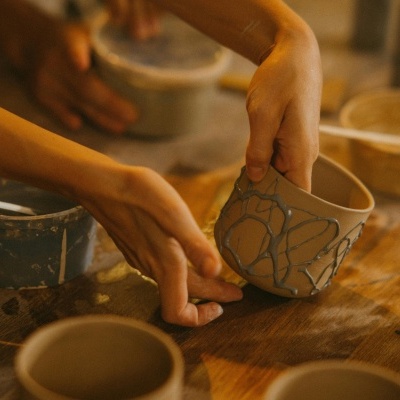 Taça de cerâmica pintada à mão com padrão cinzento e mãos a segurá-la sobre mesa de madeira