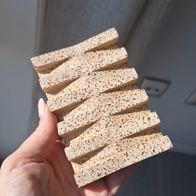 Amostra de material beige com textura granulada segurada por uma mão