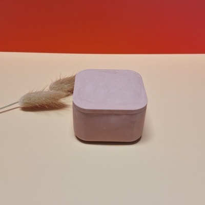 Caixa quadrada rosa com raminho seco sobre superfície bege e fundo vermelho