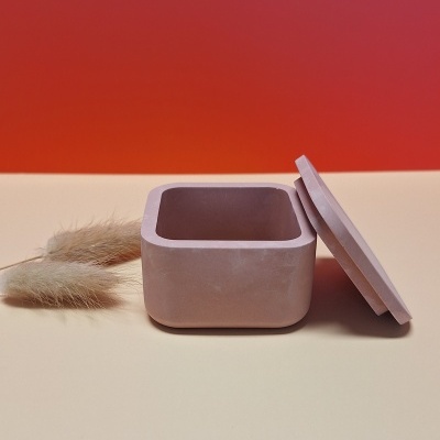 Caixa quadrada rosa em cerâmica mate com tampa ao lado sobre superfície creme