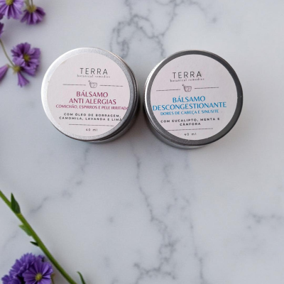 Embalagens metálicas de bálsamos anti alergias e descongestionante com flores roxas em fundo branco marmorizado