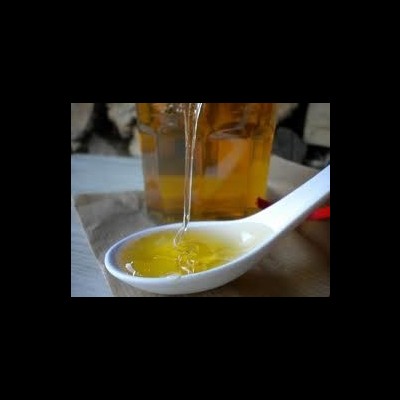 Mel dourado a ser vertido numa colher branca sobre superfície de madeira