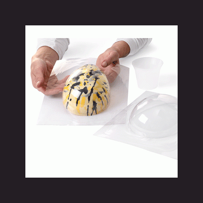 Forma de silicone transparente com objeto oval colorido em preto, amarelo e branco e copo plástico ao lado.