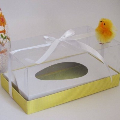 Caixa de embalagem amarela e branca com tampa transparente e pintainho de pelúcia amarelo no topo