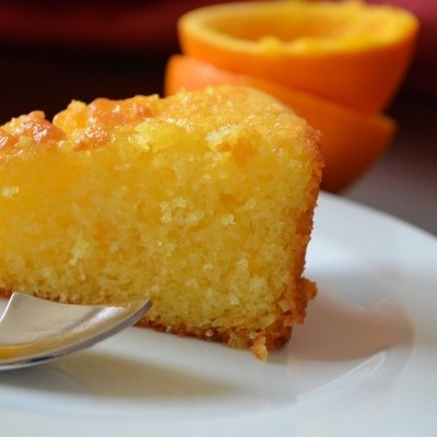 Fatias de bolo amarelo húmido num prato com laranjas ao fundo