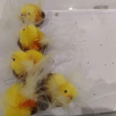 Brinquedos decorativos de pintinhos amarelos com penas brancas colocados numa superfície branca