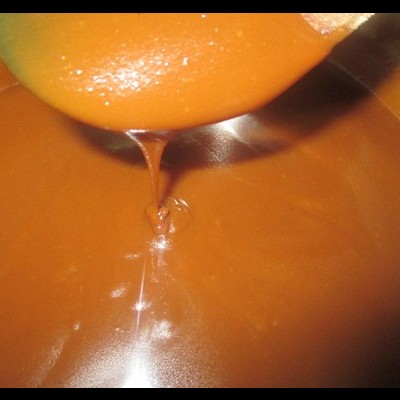 Substância castanha espessa a escorrer de uma espátula laranja num recipiente metálico