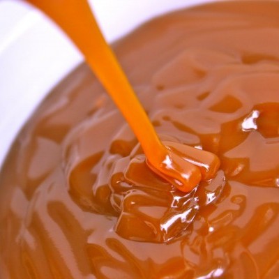 Caramelo líquido laranja a ser derramado sobre superfície lisa e brilhante.