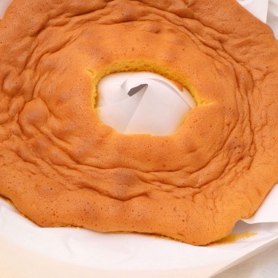 Bolo tipo rosquilha laranja claro sobre papel branco.
