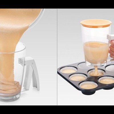 Medidor transparente com massa bege sendo despejado em formas de silicone numa bandeja para muffins.