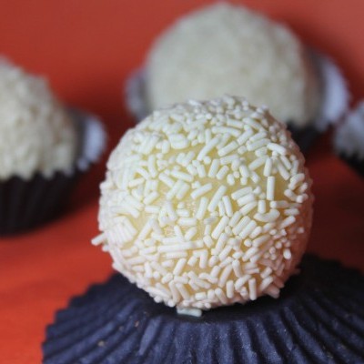 Brigadeiro branco coberto com granulados em forminha preta com fundo laranja