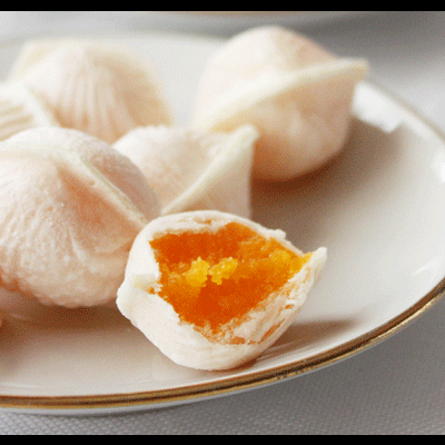 Doces tradicionais brancos com recheio laranja num prato branco com borda dourada.