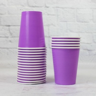 Copos de plástico roxos empilhados e dispostos sobre superfície branca com fundo de parede de tijolos brancos.