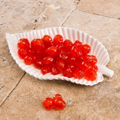 Taça branca formato folha com cerejas cristalizadas vermelhas sobre pedra clara