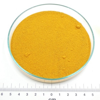 Pó amarelo alaranjado fino em prato de vidro sobre fundo branco com régua em centímetros.