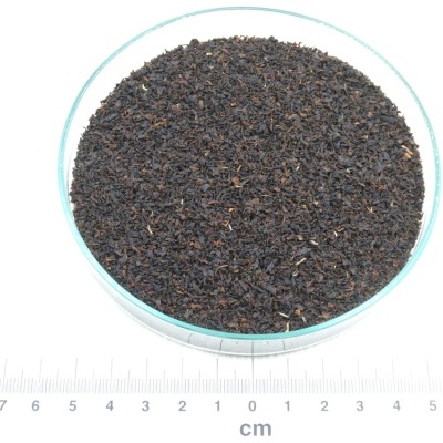 Ervas secas castanho-escuras numa taça de vidro sobre superfície branca com régua