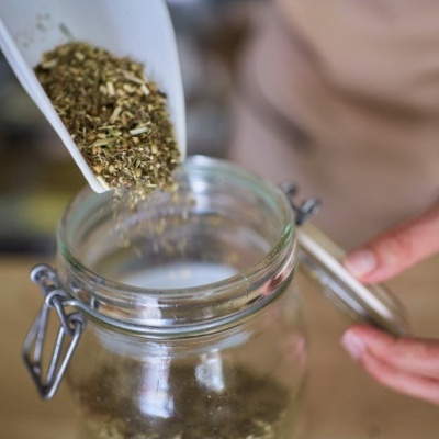 Frasco de vidro sendo enchido com ervas secas