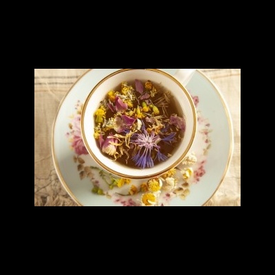 Xícara de chá com flores secas em pires floral sobre mesa de madeira