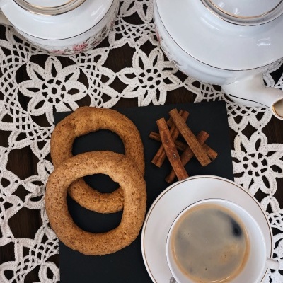 Conjunto de chá com bule, chávena de café, biscoitos e paus de canela sobre toalha branca de renda.