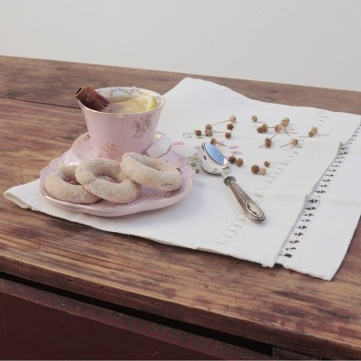 Xícara e pires rosa com biscoitos sobre toalha branca numa mesa de madeira