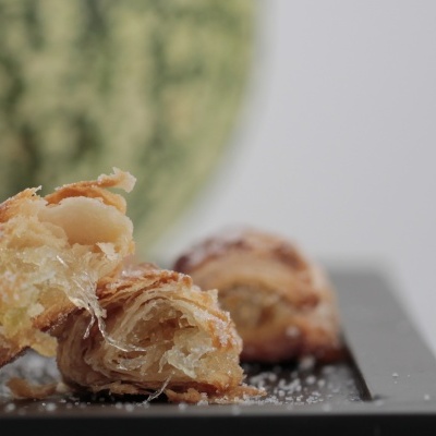 Pedaços de folhado com açúcar em pó em superfície preta, melancia ao fundo desfocada