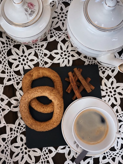 Conjunto de chá com bule, chávena de café, biscoitos e paus de canela sobre toalha branca de renda.