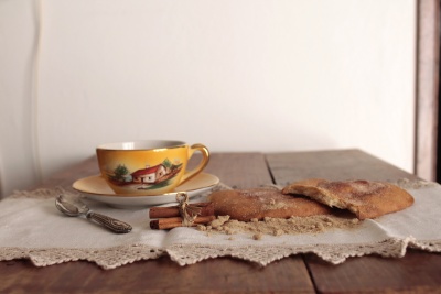 Conjunto de taça e prato amarelos com ilustração, faca decorada, pão rústico e toalha branca numa mesa de madeira.