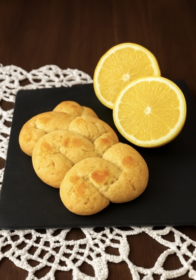 Bolachas amarelas em formato trançado com duas metades de limão em base preta sobre toalha de renda branca