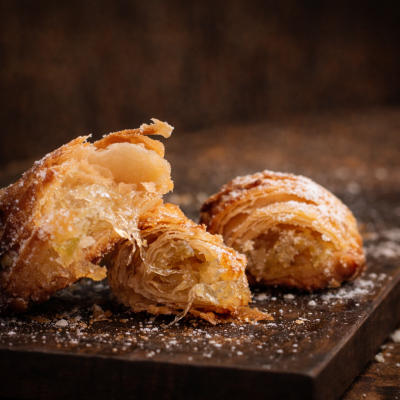 Dois pastéis folhados dourados polvilhados com açúcar em pó em tabuleiro de madeira