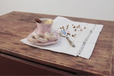 Xícara e pires rosa com biscoitos sobre toalha branca numa mesa de madeira