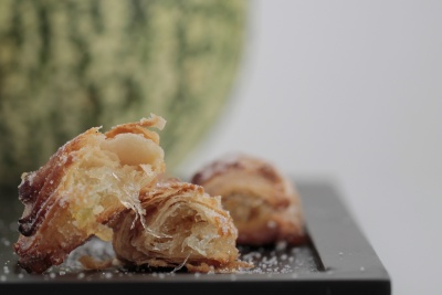 Pedaços de folhado com açúcar em pó em superfície preta, melancia ao fundo desfocada