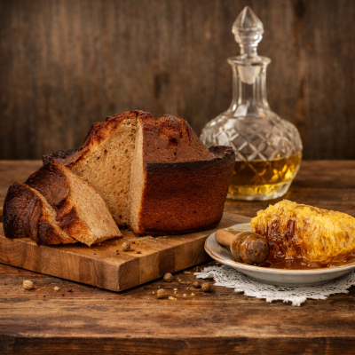 Pão rústico fatiado, favo de mel e garrafa de vidro com líquido dourado sobre mesa de madeira