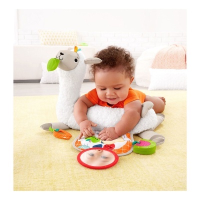 Bebé com brinquedo macio em forma de lhama branco e acessórios coloridos sobre tapete amarelo