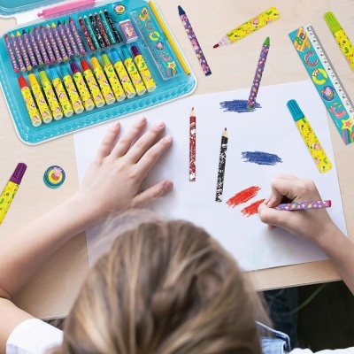 Criança a desenhar com lápis de cera coloridos em mesa com conjunto de desenho