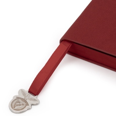 Caderno vermelho com marcador de fita e pendente metálico com emblema